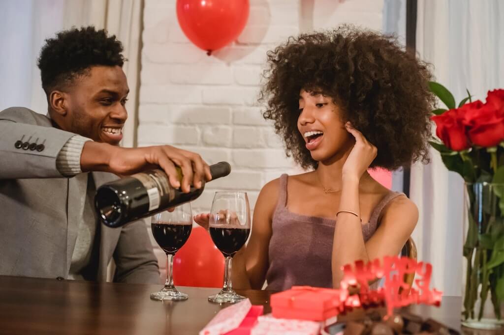 man pouring wine into woman's wine glass and smiling. 